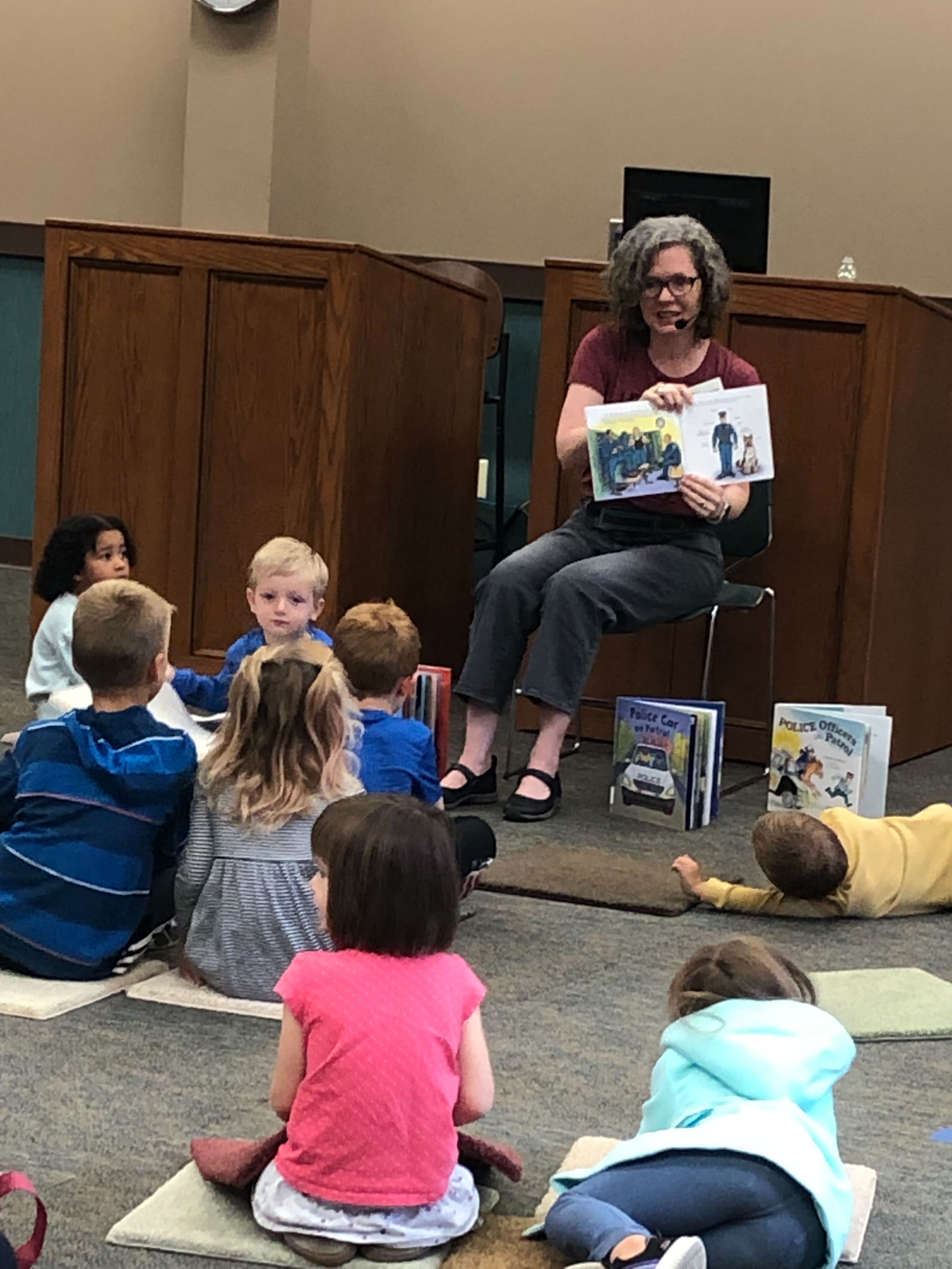 A woman holds a book during a read aloud to young children and their adults.