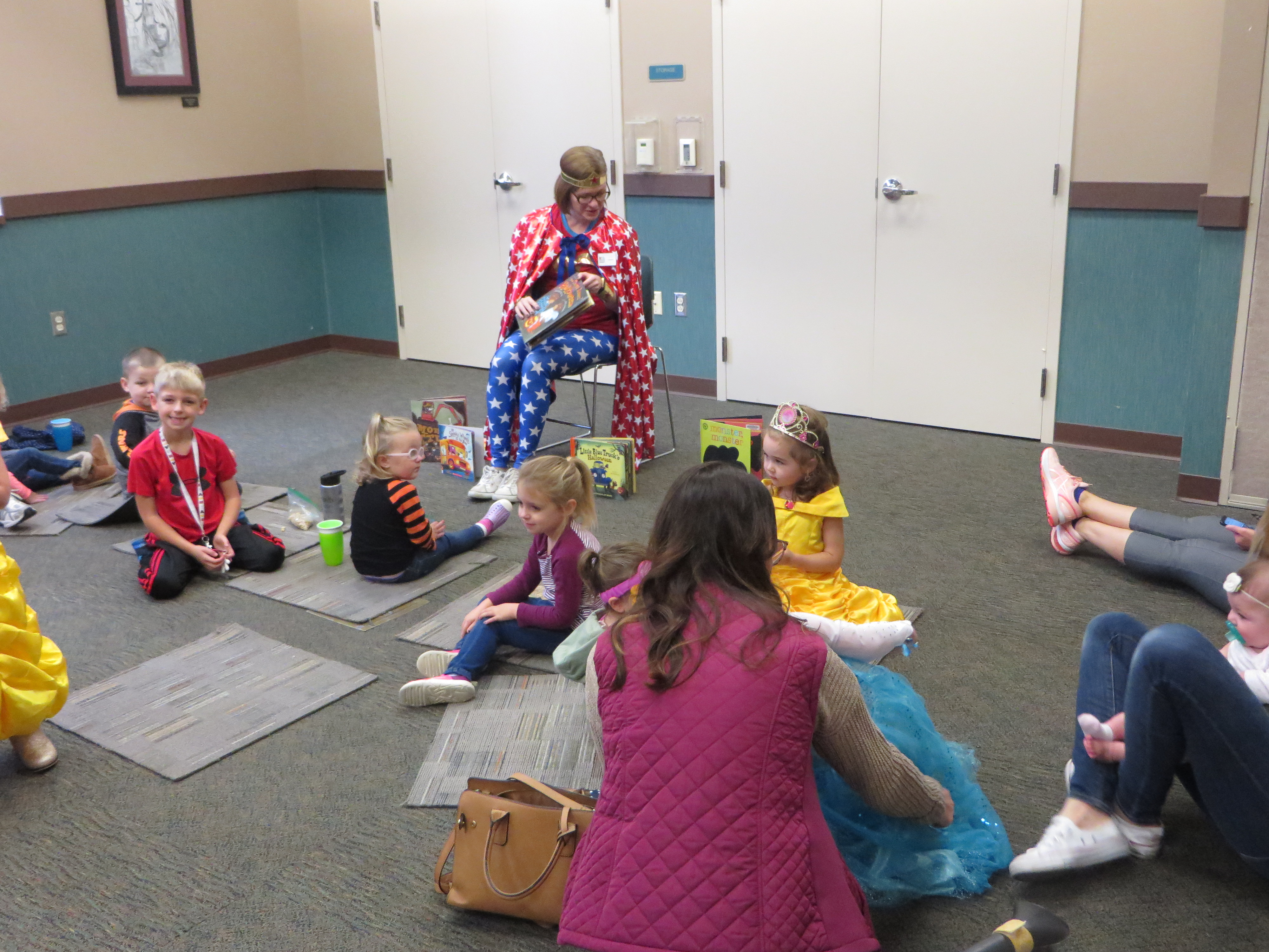 A woman dressed up in red, white and blue with stars reads to small children in costume.