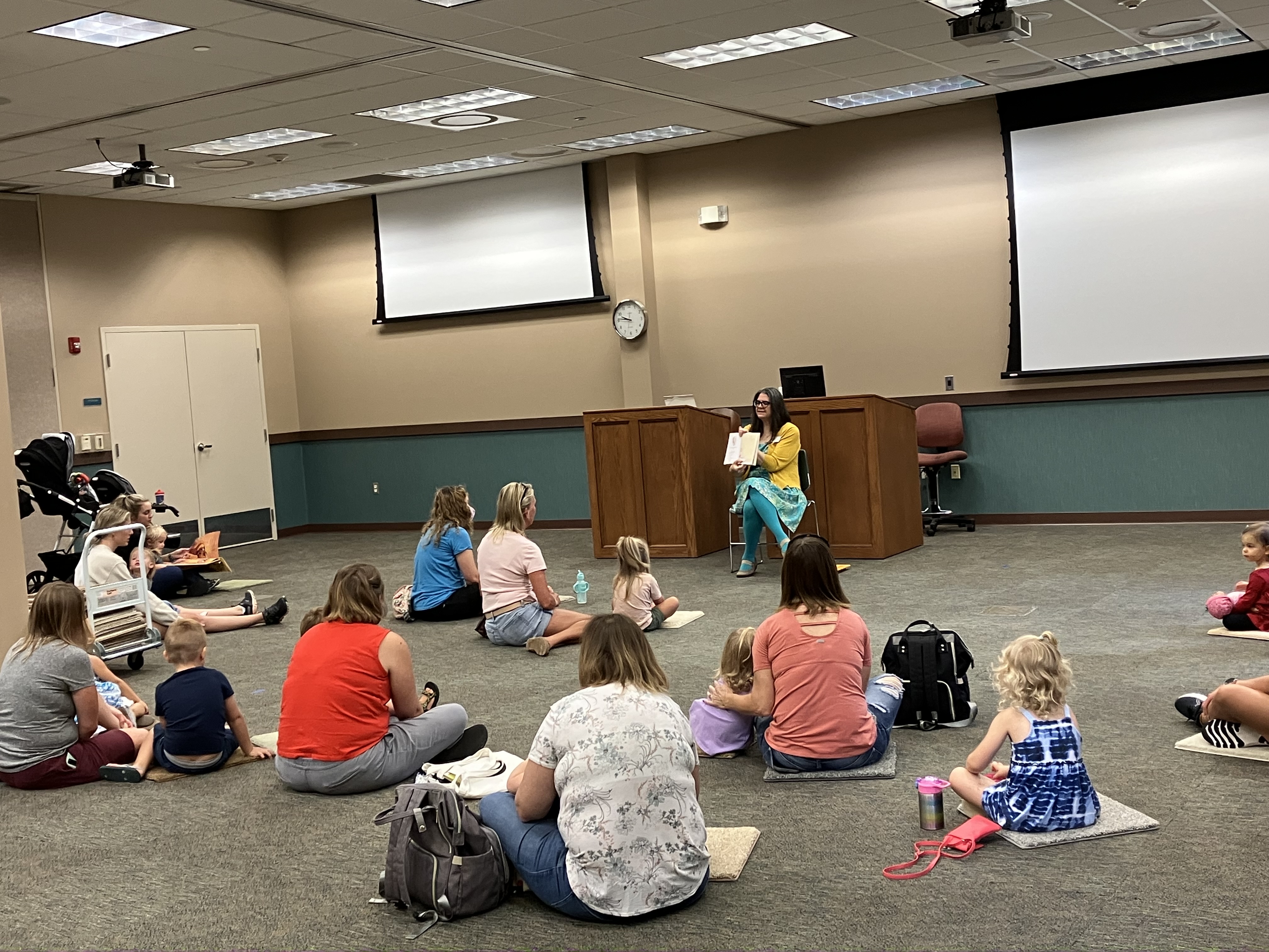 A woman holds a book during a read aloud to young children and their adults.