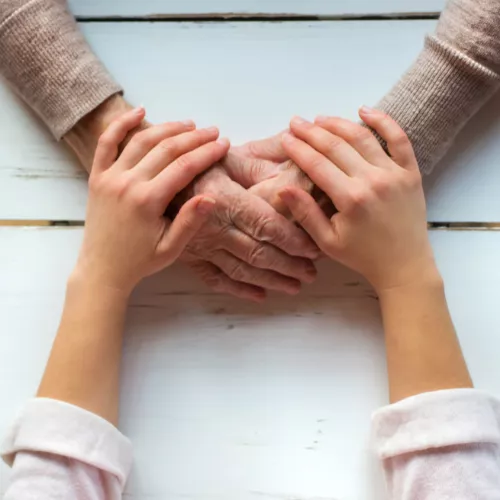 young person&#039;s hands covering a older adult&#039;s hands that are clasped