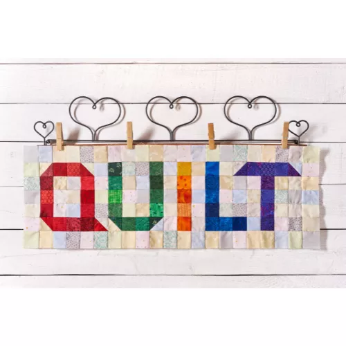 The word quilt spelled out in quilt block.  Each letter is the colors of the rainbow